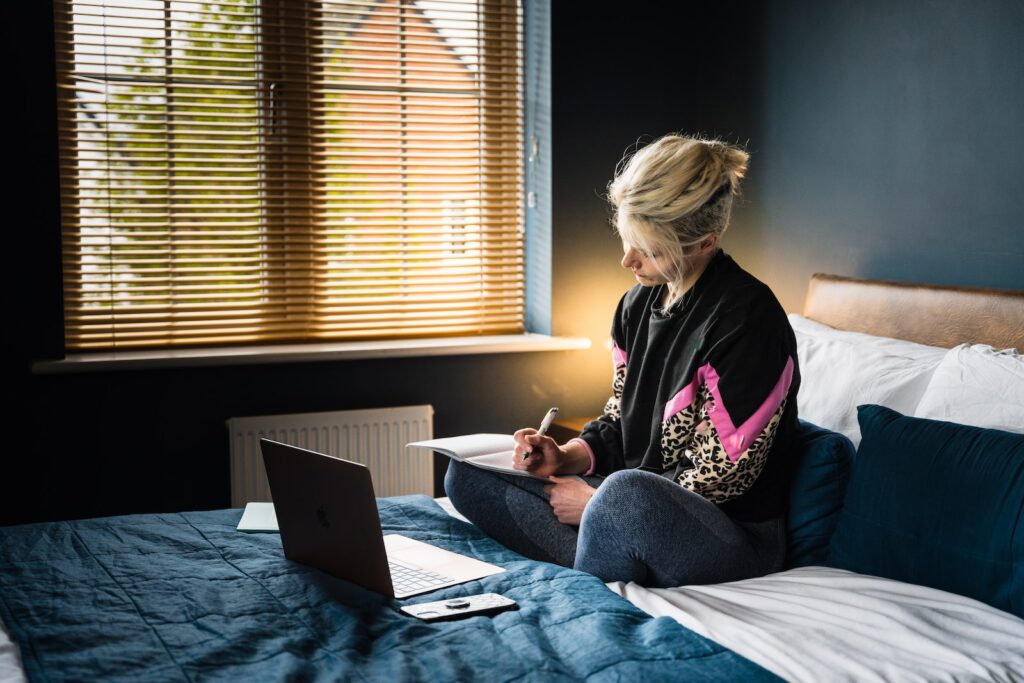 Minnesota woman in purple and white floral long sleeve shirt and gray pants sitting on bed creating a safety plan