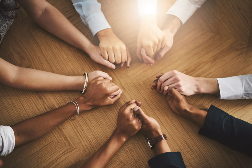 Closeup shot of a group of people sitting together at a table and holding hands.