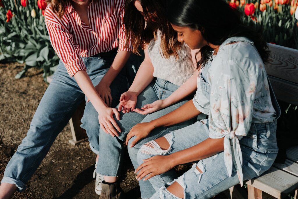 Three Minnesota women wearing blue denim jeans sitting on gray wooden bench helping someone else through domestic violence 