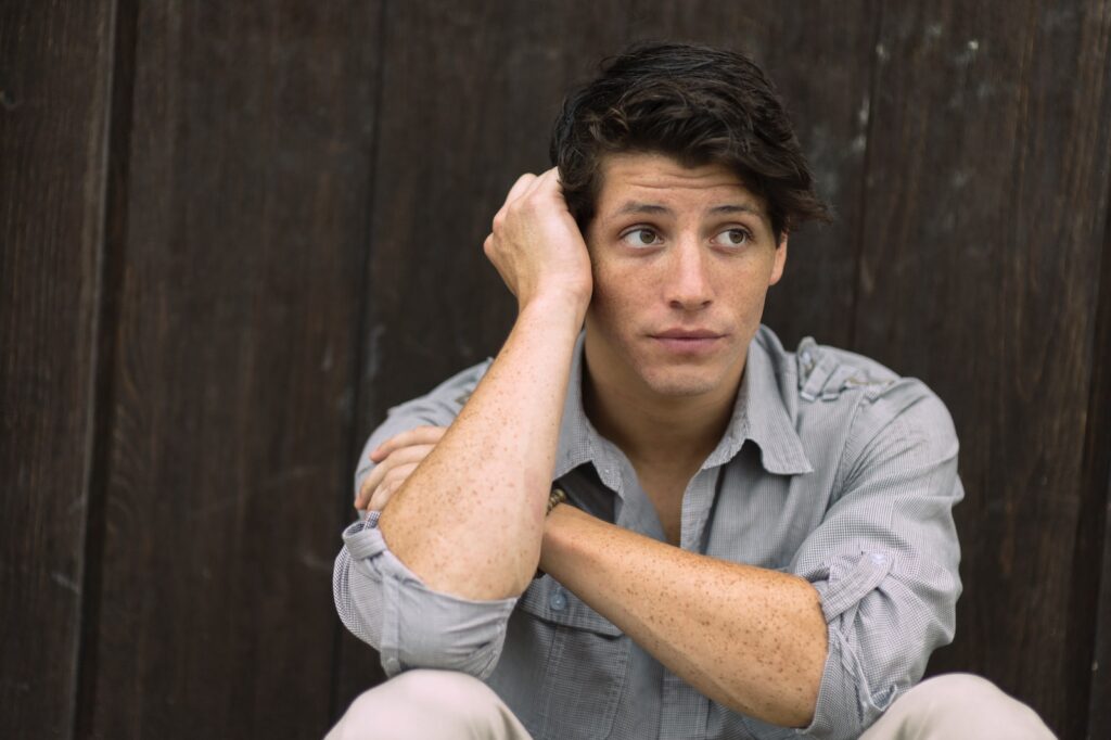 Minnesota man who survived sexual violence wearing gray dress shirt leaning on brown wall